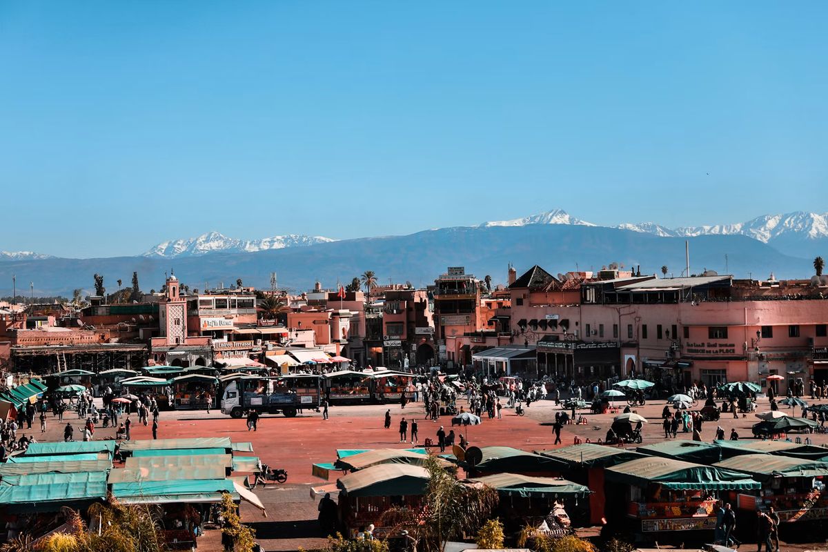 Der Jemaa el-Fna mit Marktständen, dahinter die verschneiten Gipfel des Atlas