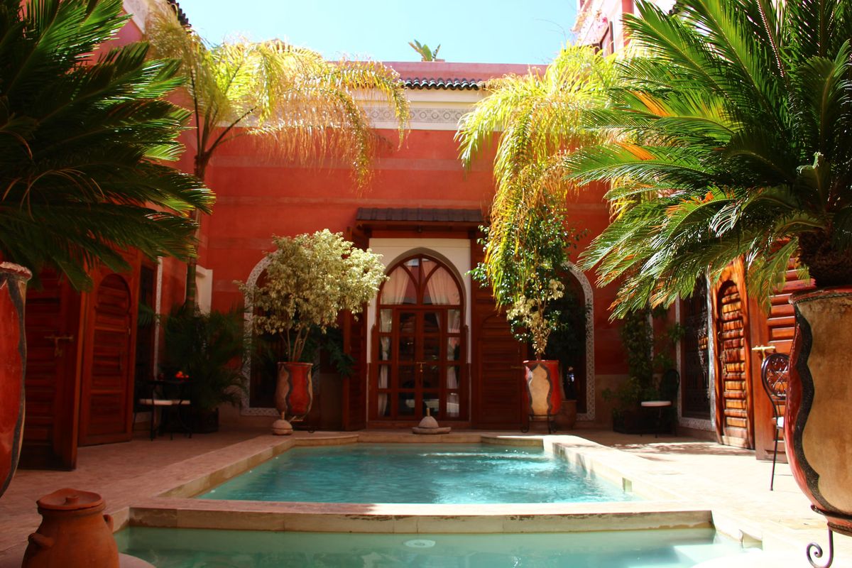 Innenhof eines Riads in Marrakesch mit roten Wänden, Palmen und Pool